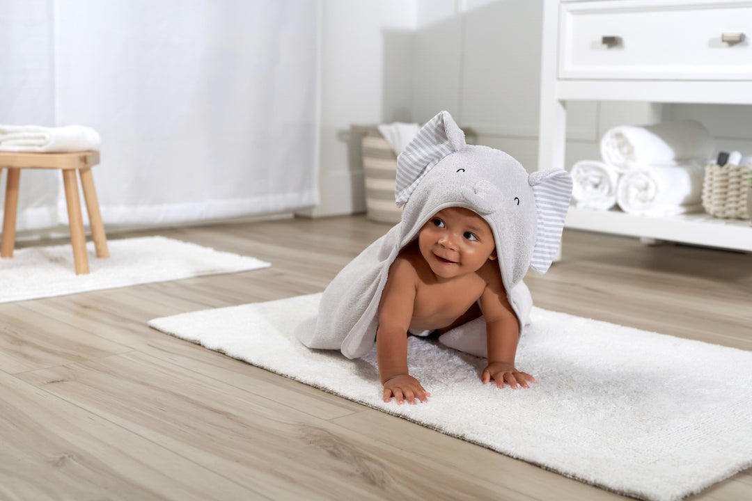 A happy baby in a snuggly elephant bathrobe, cuddled up on a soft rug ready for post-bath snuggles.
