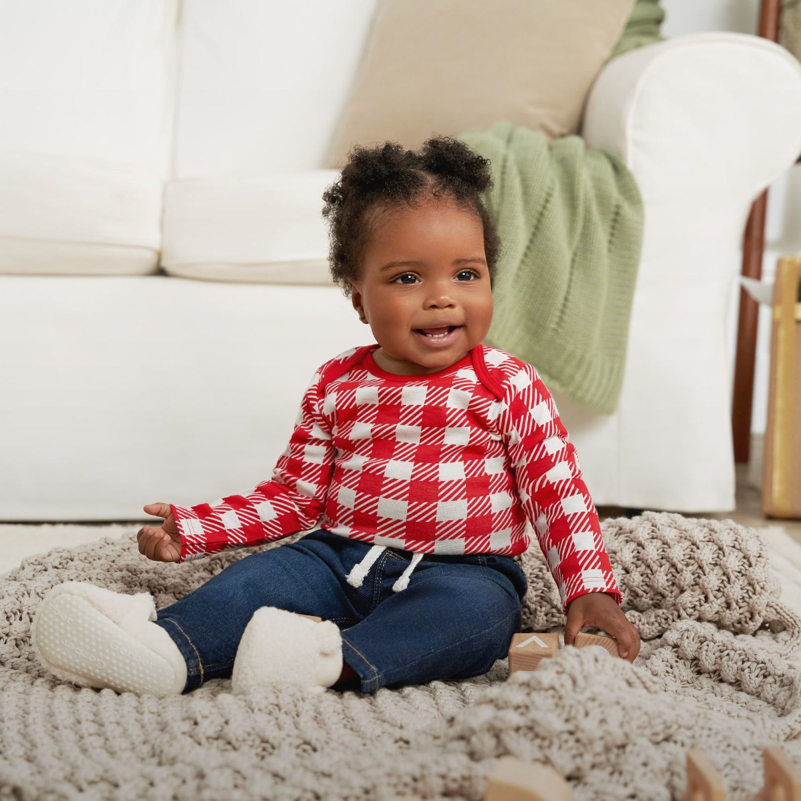  A young African American child sits on a rug wearing a red and white plaid shirt.