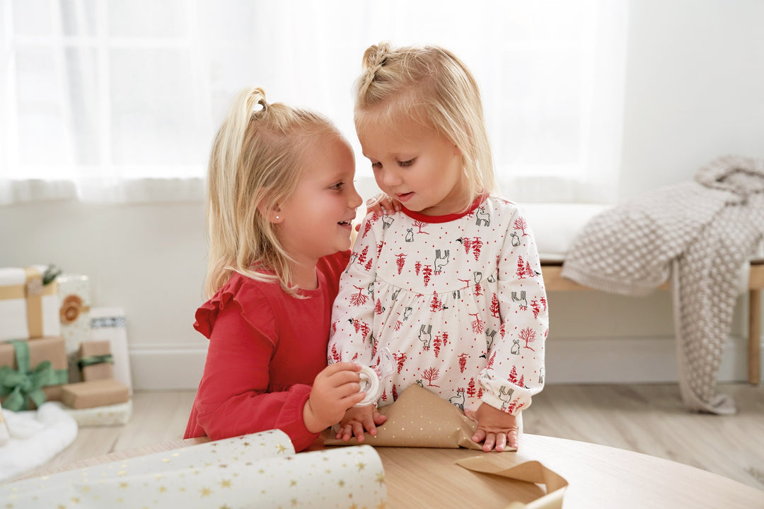 Two little girls in matching new arrivals sitting on a table, sharing a moment of joy and friendship.